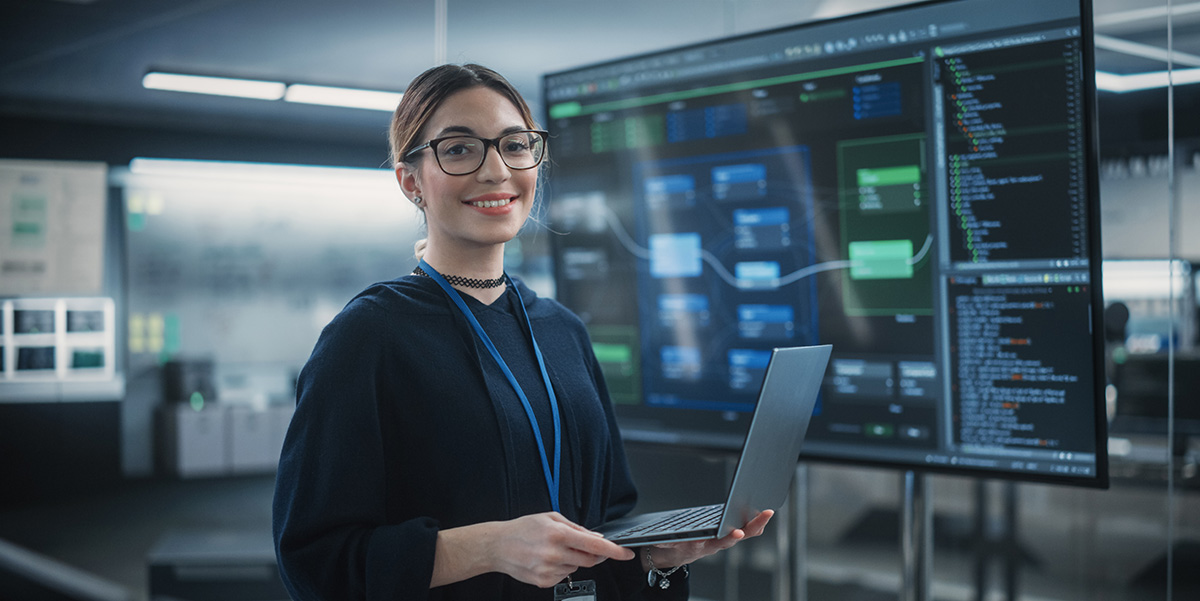 Young smiling woman standing in front of a mainframe room with laptop in hand