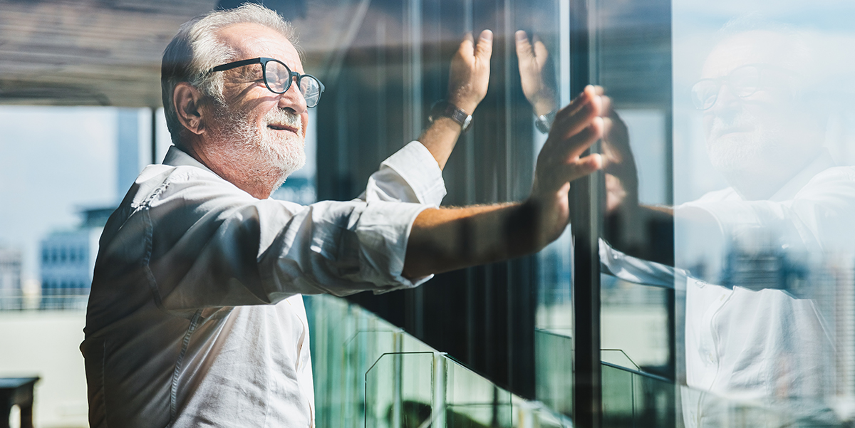 Man with white hair in his 60ies looking out of a glass window in a fancy office tower.