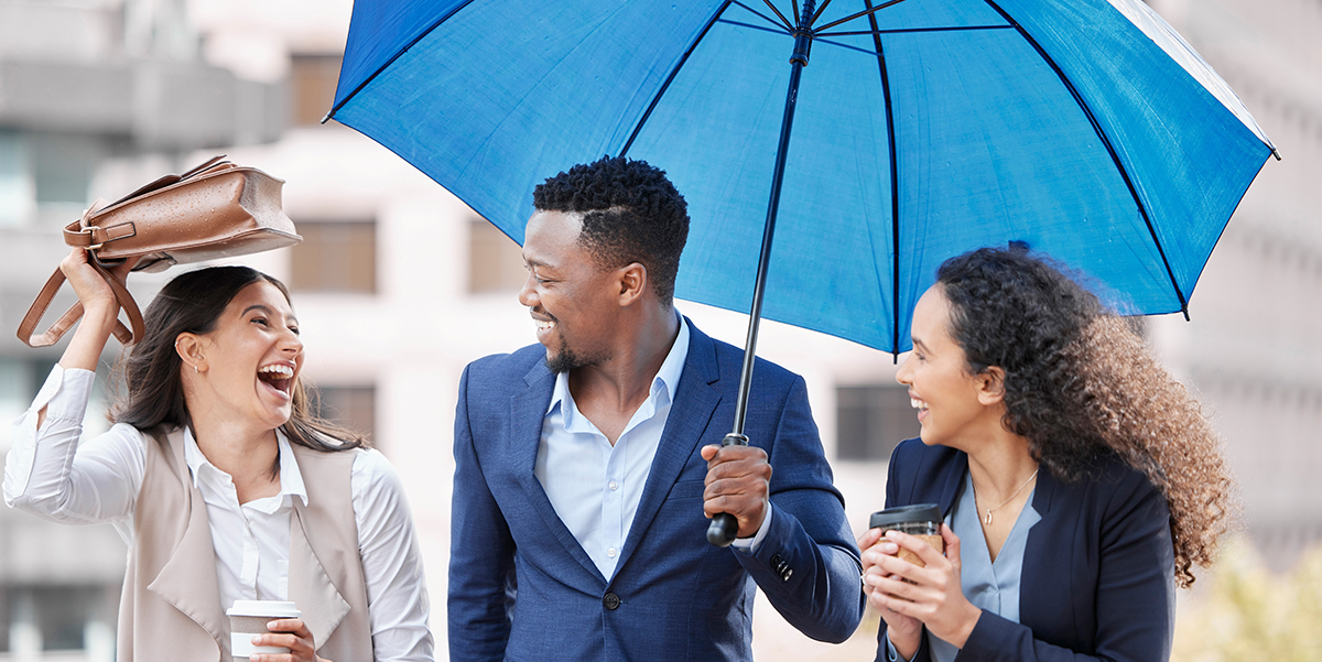 Man and twor women under a blue umbrella protected form the rain.