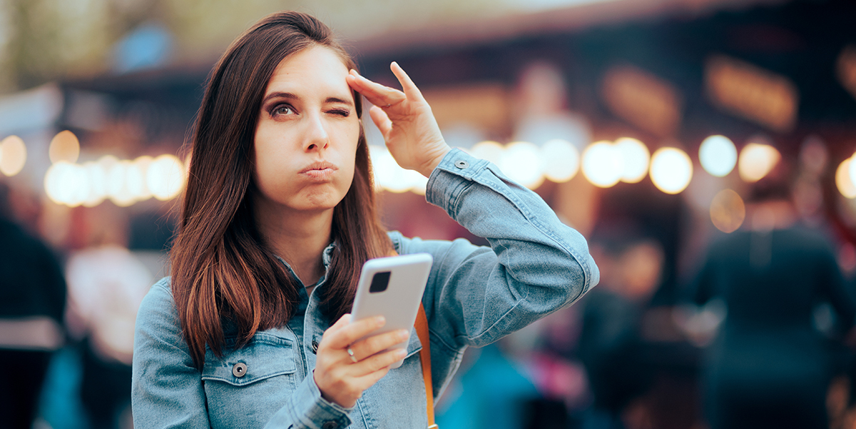 Woman with cellphone with facial expression of puffing air while massaging one side or her temple