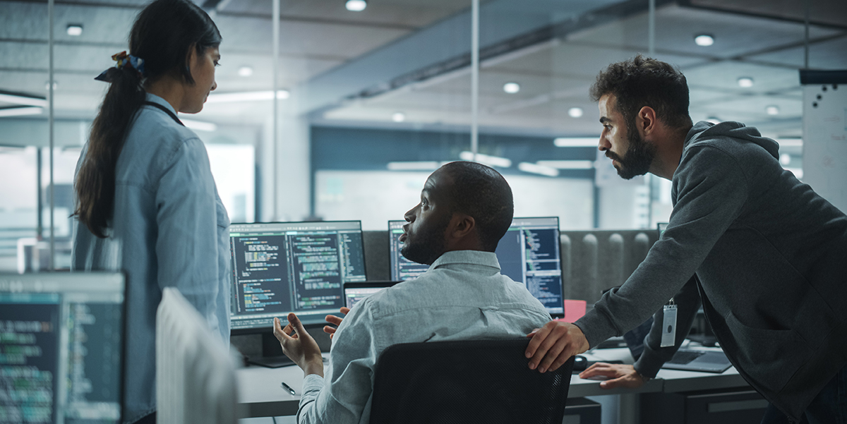 Two male and one female worker taling in front of computers in a climate controlled server room.