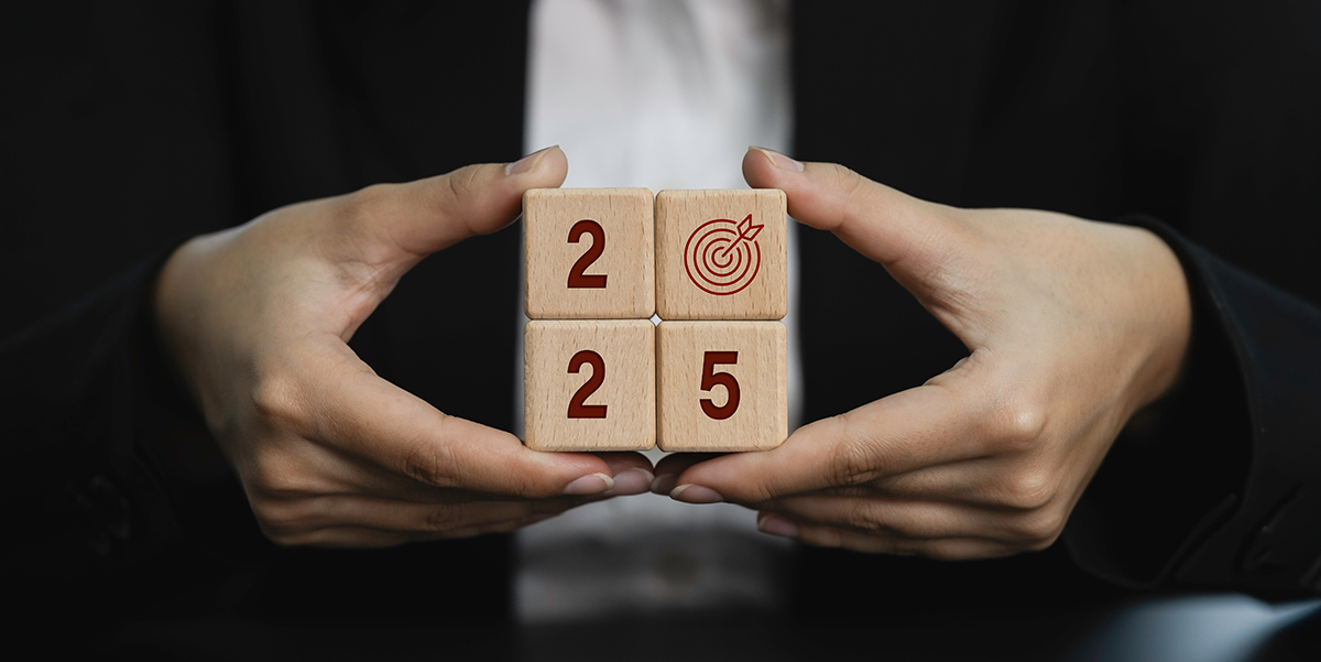 Male hands holding four wooden cubes with the numbers 2025. The number 0 is a red bullseye.