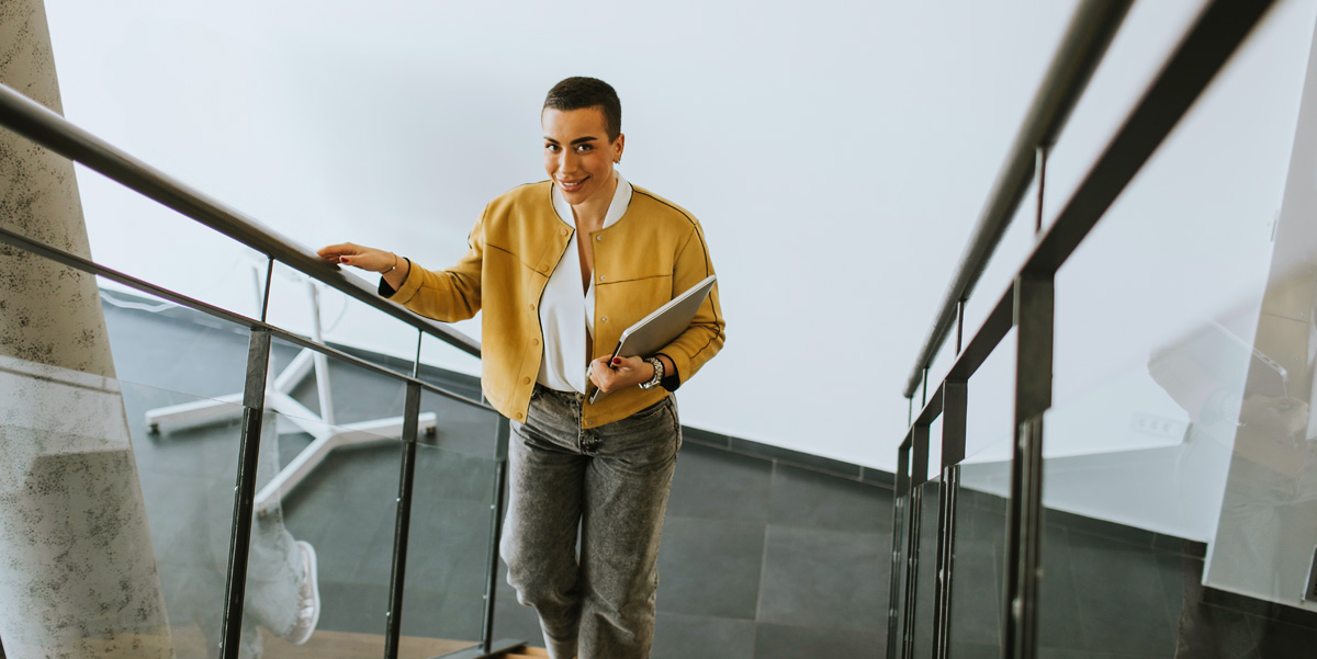 Woman with her laptop accending modern office stairs.