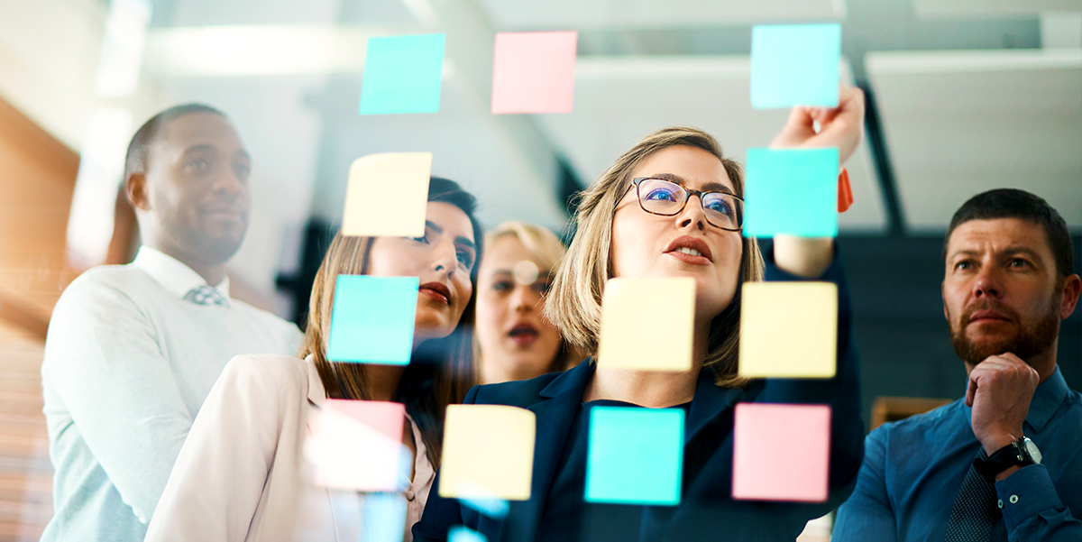 A team of employees in front of a class wall with post-it notes working on a strategy