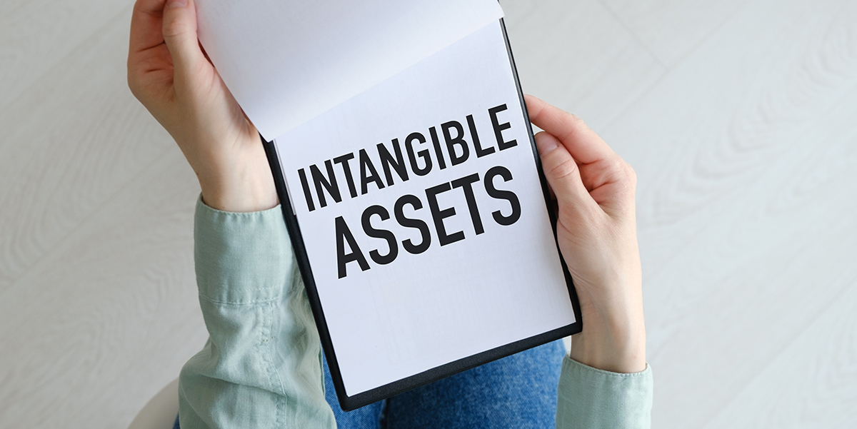 Person holding a note pad with white paper and the words "intangible assets.”