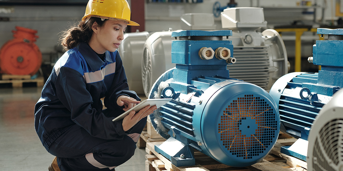 Woman with hard hat looking at clip board in front of machinery.